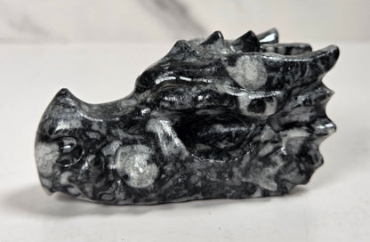 A carved black and white marbled stone dragon head figurine, photographed on a light gray surface with a marble-patterned background.