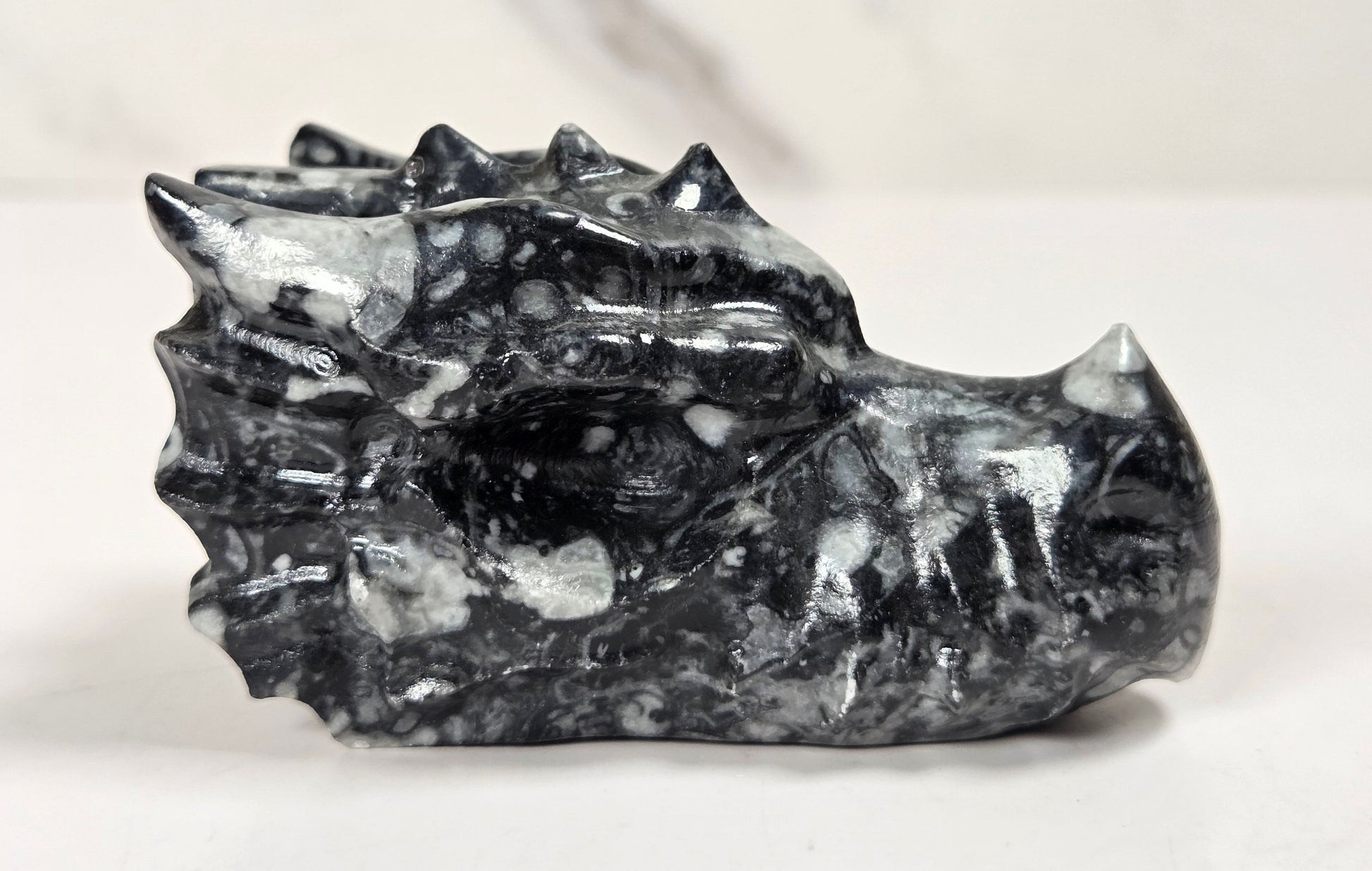 A carved black and white marbled stone dragon head figurine, displayed on a light gray surface against a white marble background.