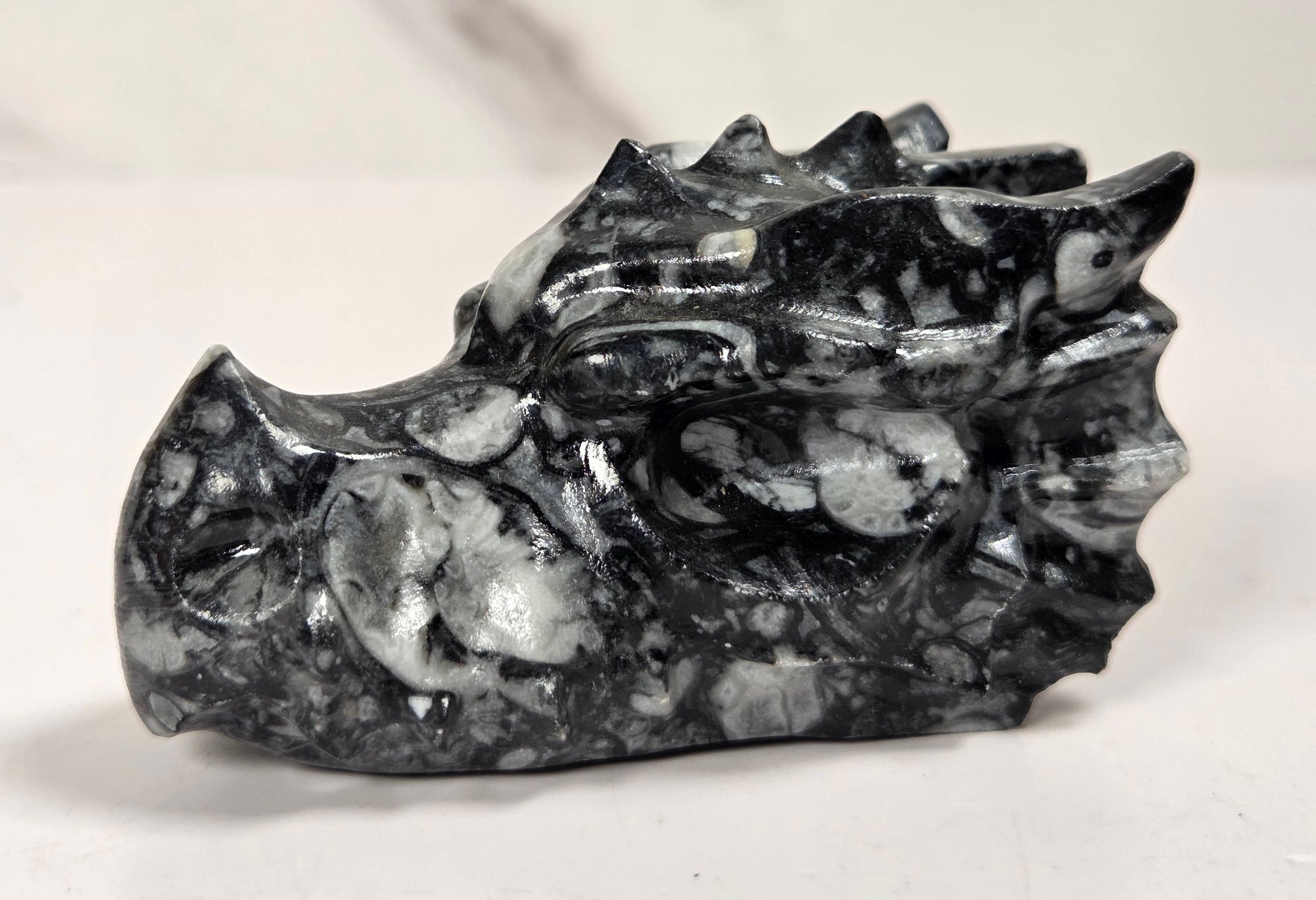 A small carved stone dragon head figurine in polished black and white marbled stone, shown on a light surface with a soft-focus marble background.