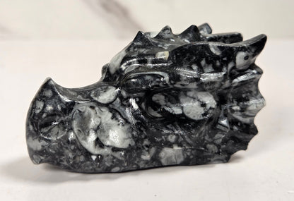 A small carved stone dragon head figurine in polished black and white marbled stone, shown on a light surface with a soft-focus marble background.