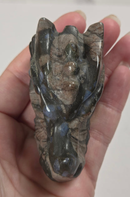 A polished crystal carving shaped like a stylized face, held in a person's hand against a light gray background.