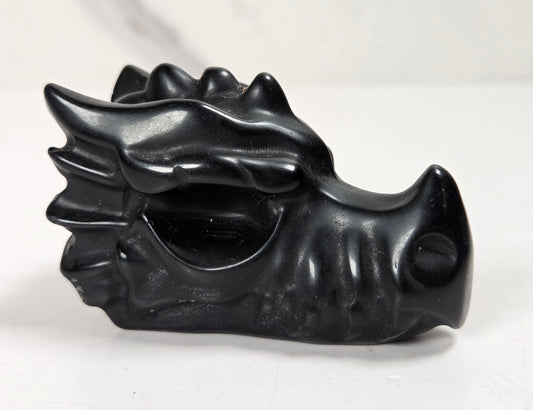 A small black dragon head figurine or decorative object with a glossy finish, photographed on a light neutral surface and background.