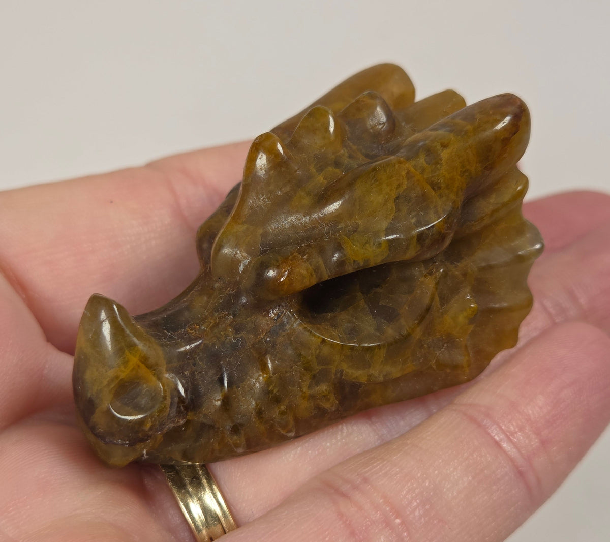 A small carved brown and amber stone dragon figurine held in a person's hand against a plain light background.