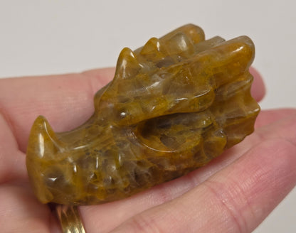 A small carved animal head pendant or charm in polished brown and amber stone, held in a person's hand against a light neutral background.