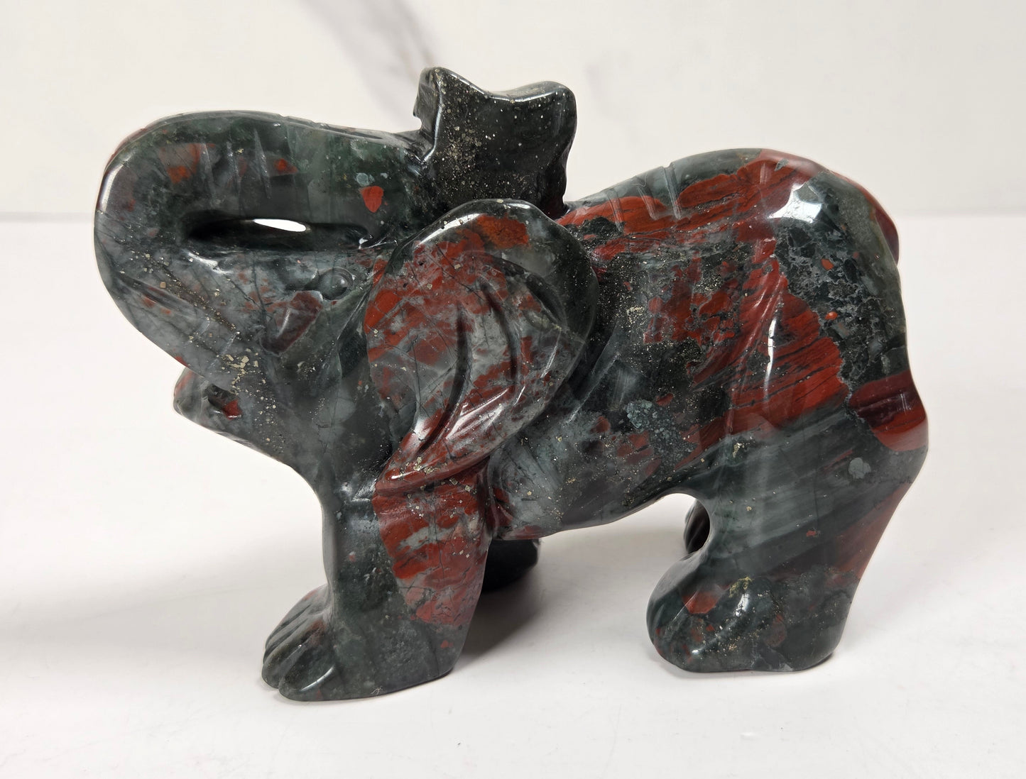 A carved elephant figurine made from polished red jasper stone, featuring a dark gray and black base with vibrant red and orange marbled patterns, set against a plain white background.