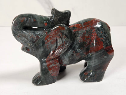 A carved elephant figurine made from polished red jasper stone, featuring a dark gray and black base with vibrant red and orange marbled patterns, set against a plain white background.