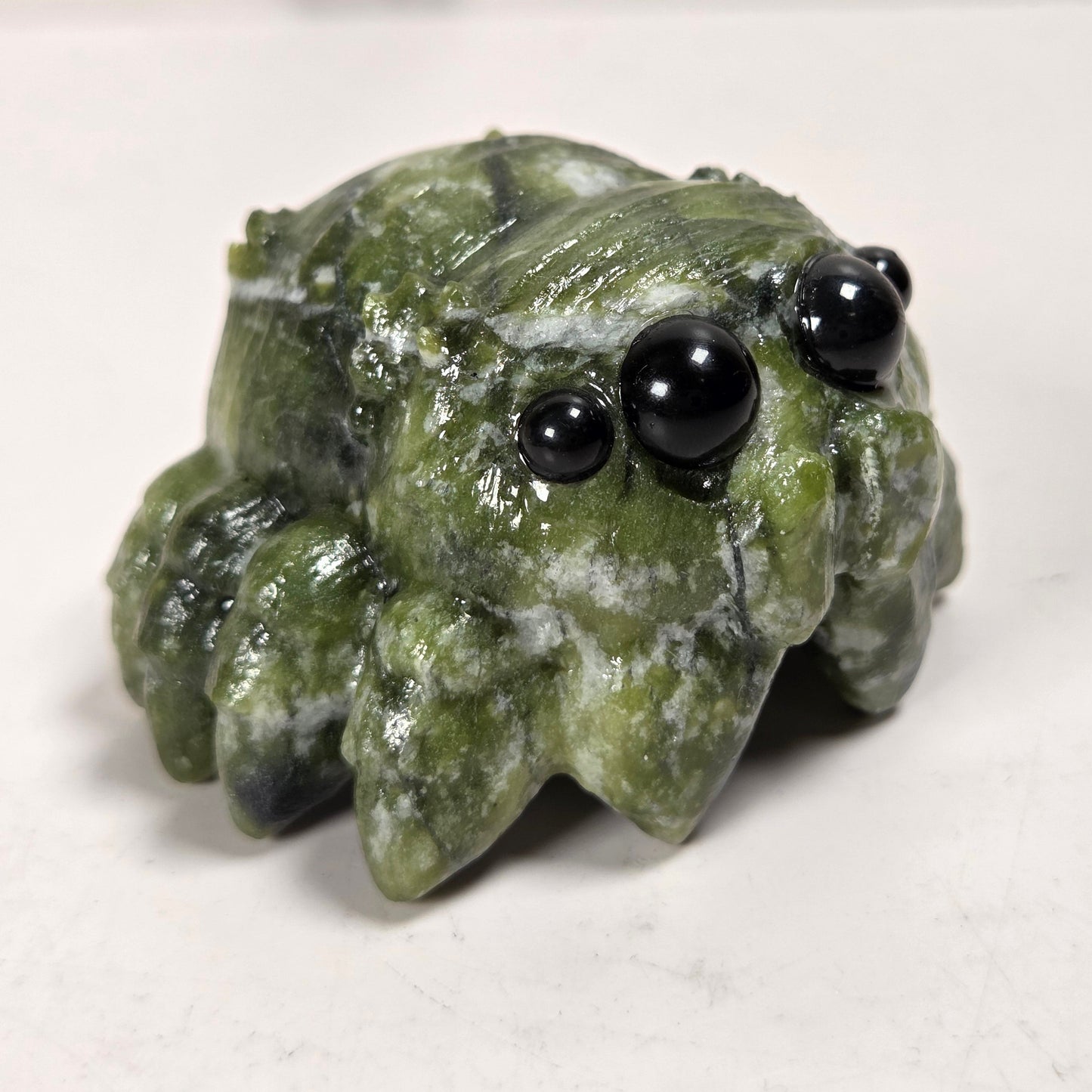 A small carved green stone creature figurine with black bead eyes, photographed on a plain light background.