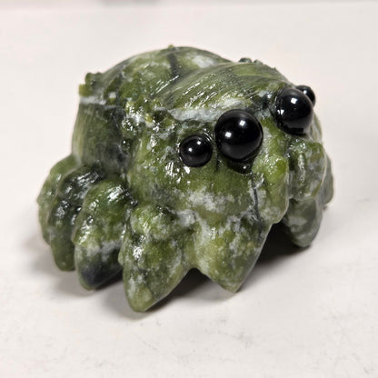 A small carved green stone creature figurine with black bead eyes, photographed on a plain light background.