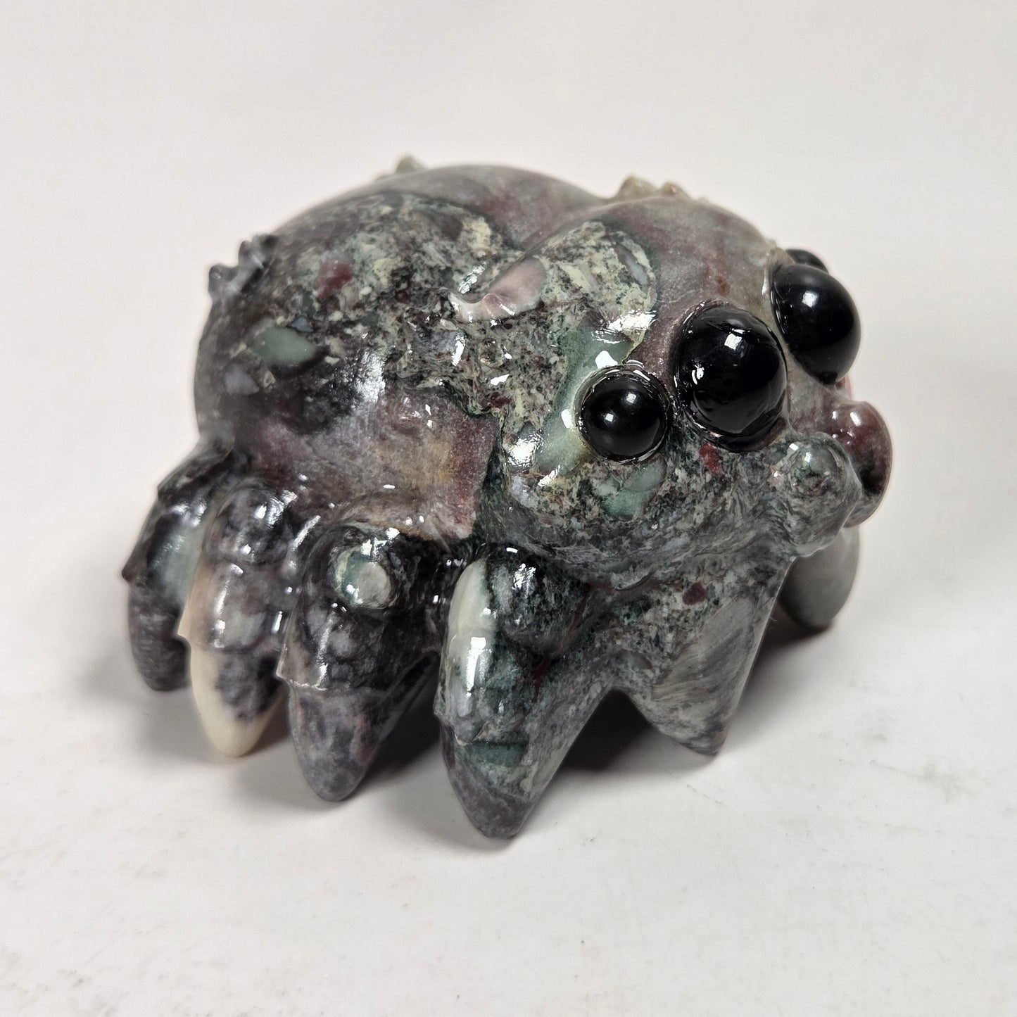 A small carved stone creature figurine with large glossy black eyes and multiple short legs, photographed on a plain light background.