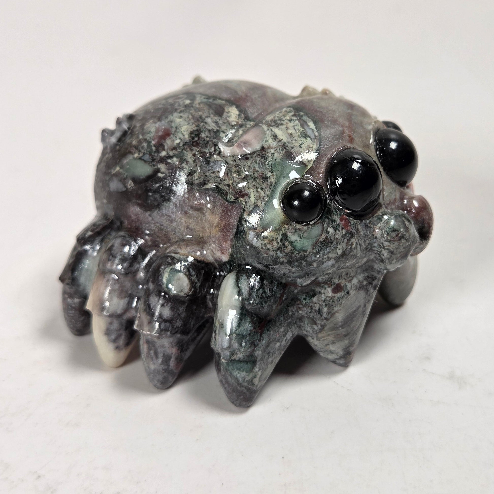 A small carved stone creature figurine with large glossy black eyes and multiple short legs, photographed on a plain light background.