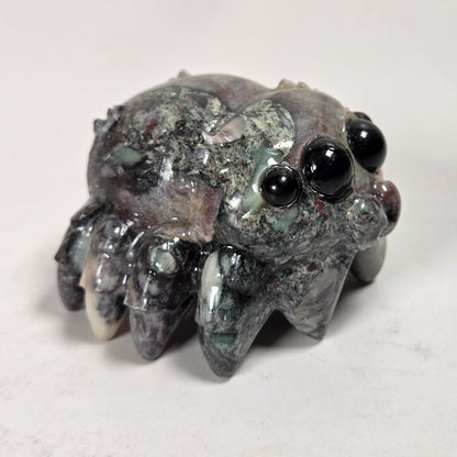 A small carved stone creature figurine with large glossy black eyes and multiple short legs, photographed on a plain light background.