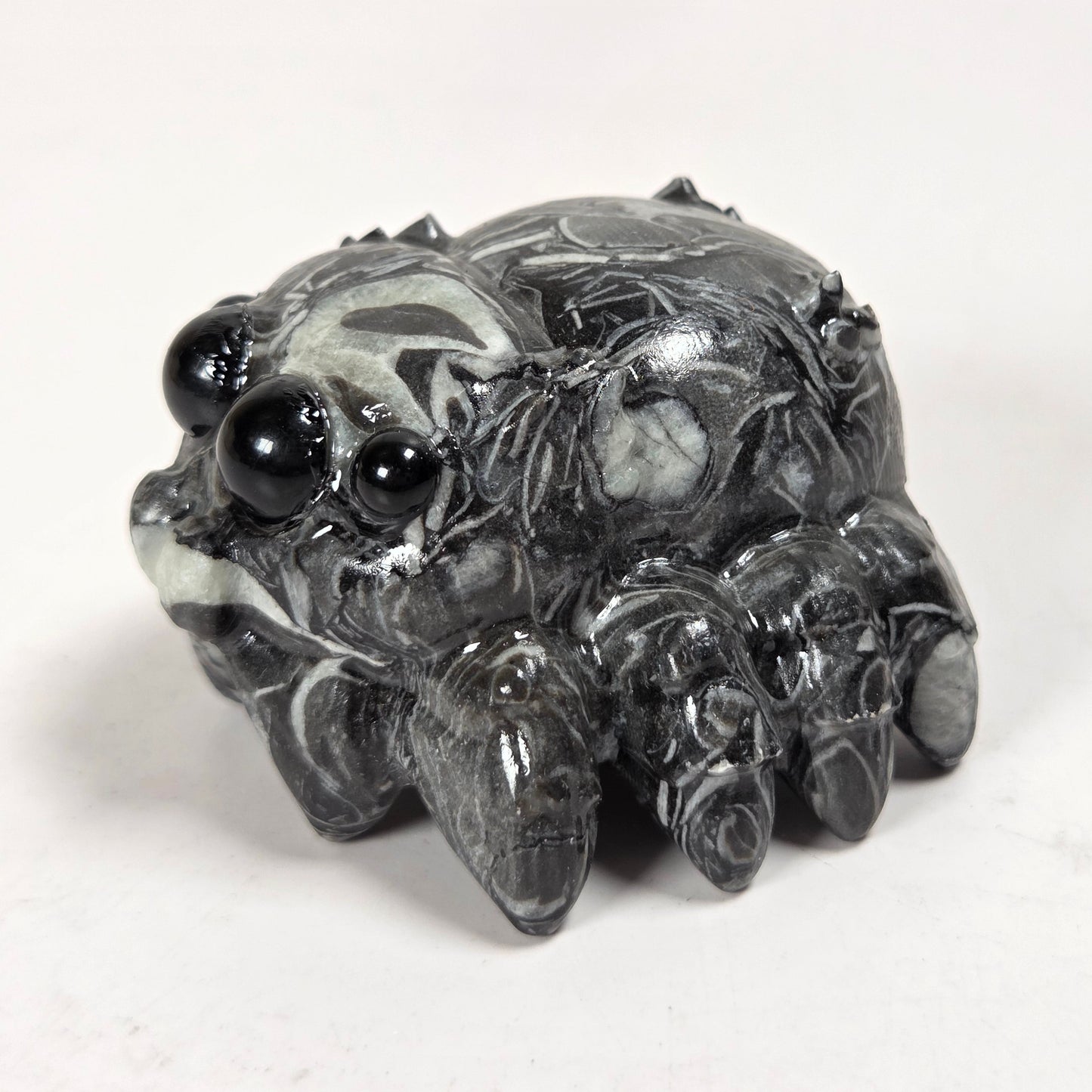 A small carved figurine of a spider, made from polished black and white marbled stone with glossy black bead eyes, set against a plain white background.