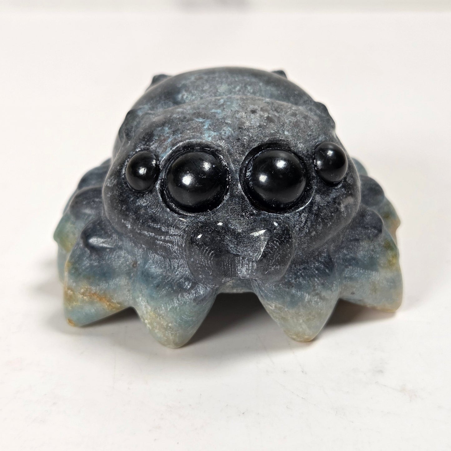 A small carved stone spider figurine with large black bead eyes, photographed on a plain light background.