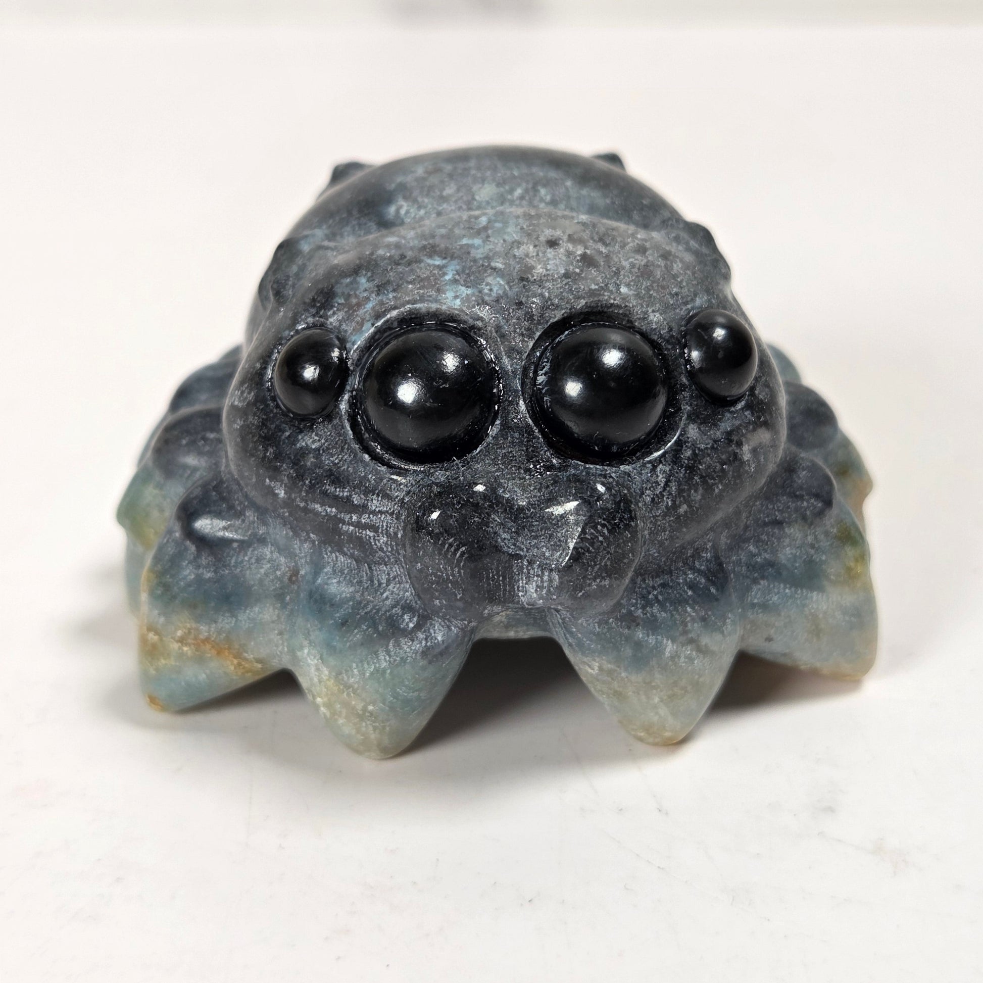 A small carved stone spider figurine with large black bead eyes, photographed on a plain light background.