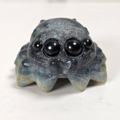 A small carved stone spider figurine with large black bead eyes, photographed on a plain light background.