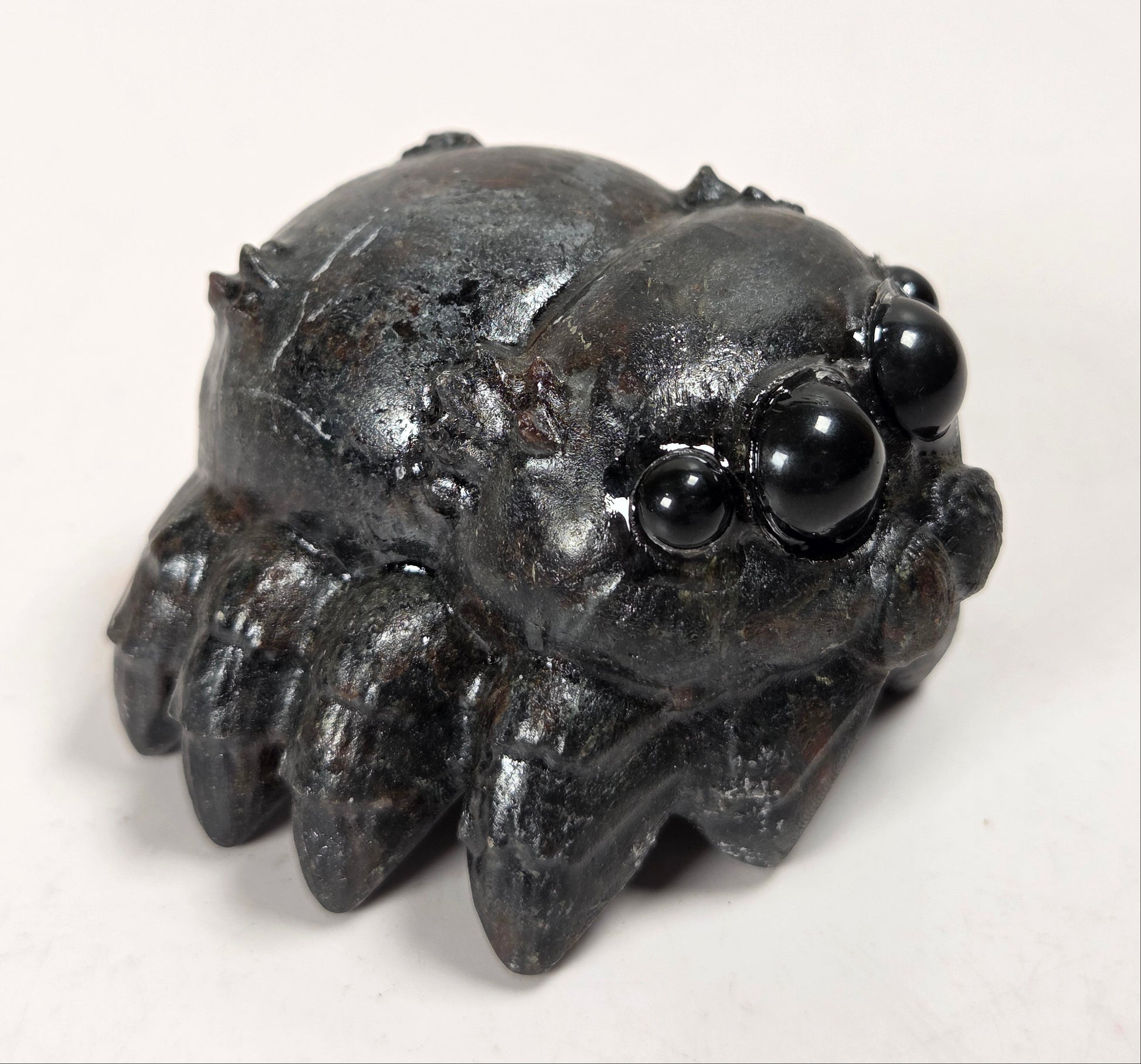 A small black spider figurine with glossy bead eyes, photographed on a plain light background.