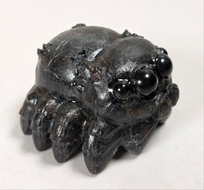 A small black spider figurine with glossy bead eyes, photographed on a plain light background.