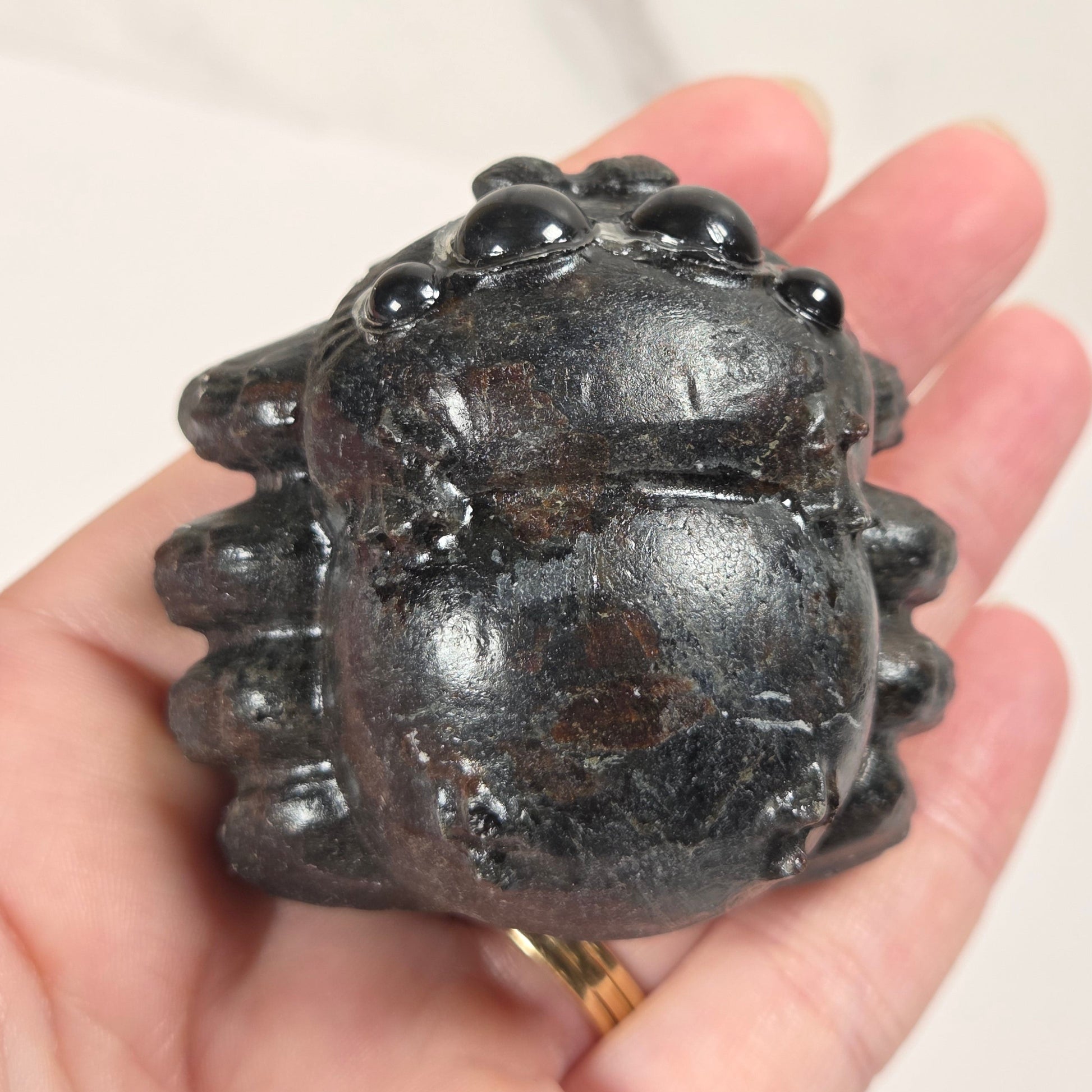 A small carved dark stone toad figurine held in a person's hand against a light marble-like background.