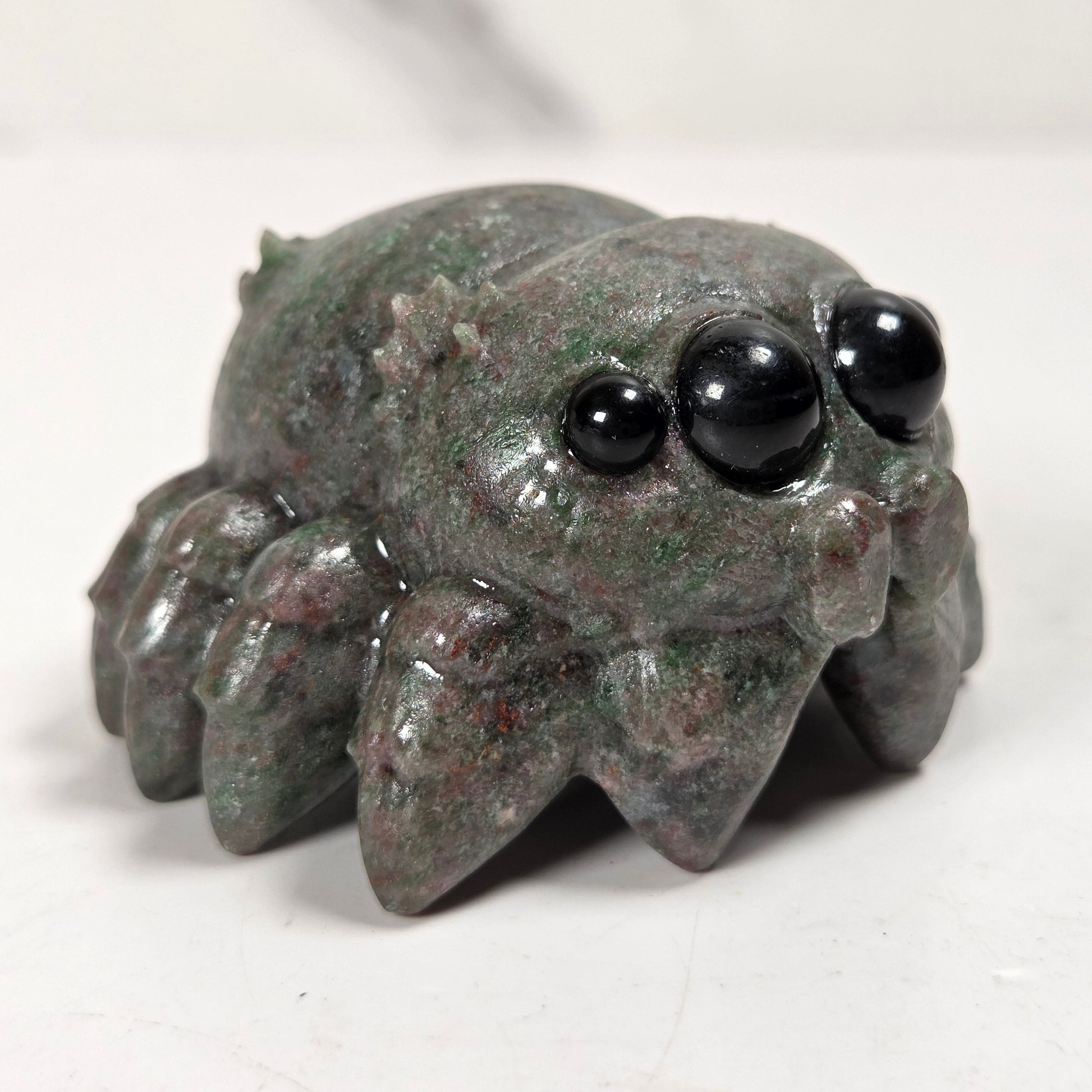 A small carved spider figurine made from polished green malachite with black bead eyes, shown on a light gray surface.
