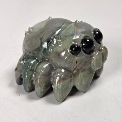 A small carved stone crab figurine with glossy black bead eyes, shown on a plain off-white surface.