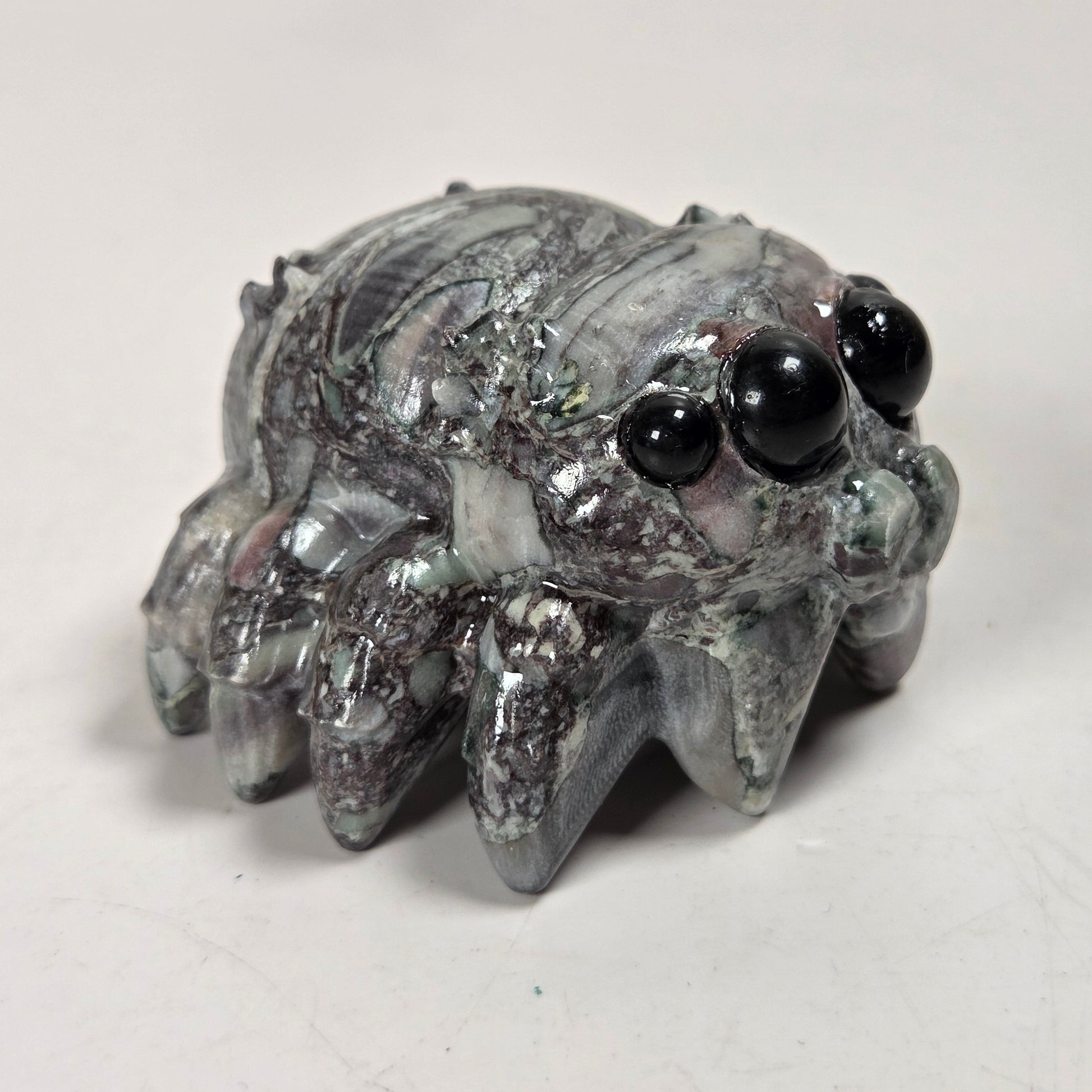 A small spider-shaped decorative object with a glossy, marbled gray and white surface and large black bead eyes, photographed on a plain light background.