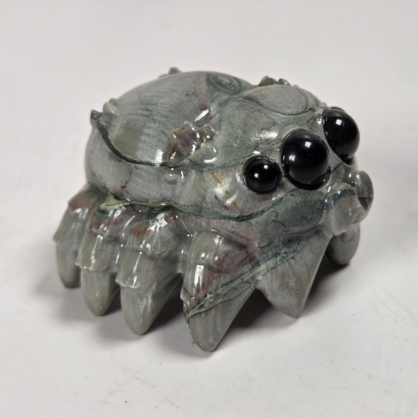 A small carved crab figurine made of polished gray stone with black bead eyes, photographed on a plain light background.