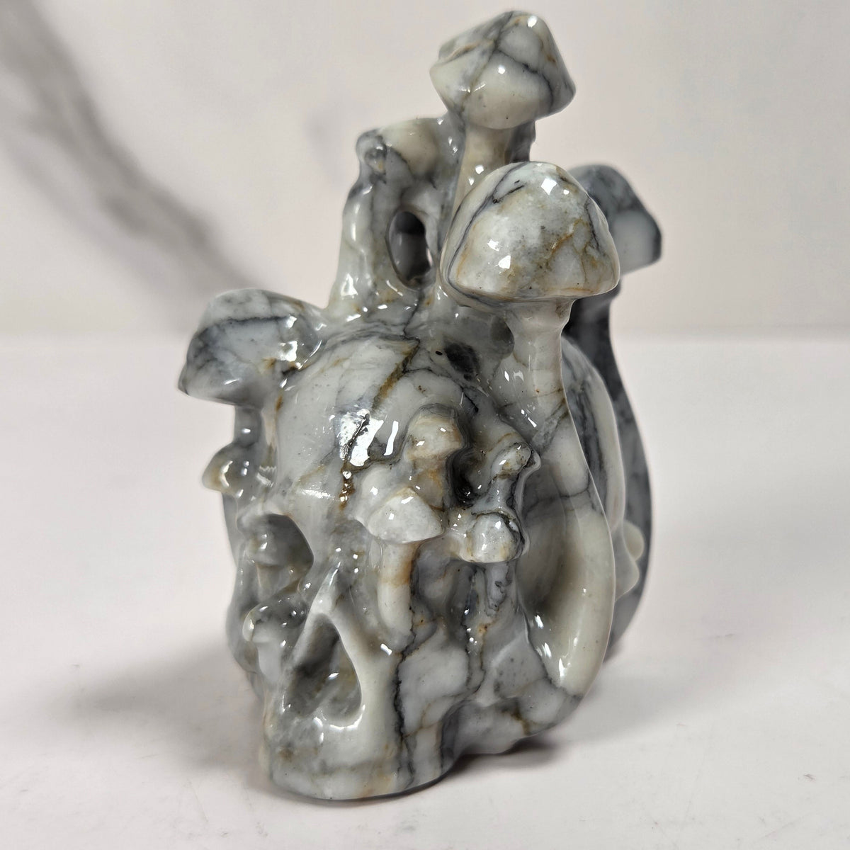 A small carved figurine of a skull with a fairy or dragon-like creature riding it, made from polished gray and white marbled stone, set against a plain light background.