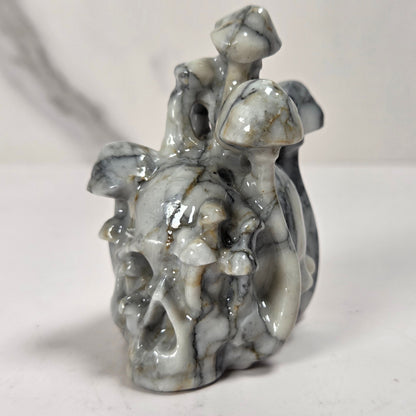 A small carved figurine of a skull with a fairy or dragon-like creature riding it, made from polished gray and white marbled stone, set against a plain light background.
