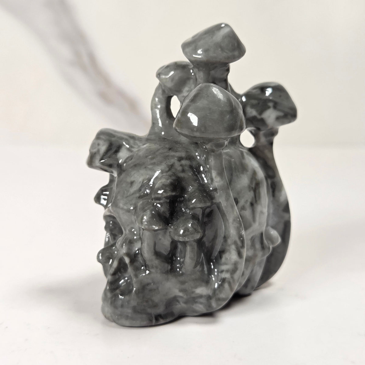 A small glossy gray sculptural figurine with a textured, organic surface, standing on a white surface against a light gray background.