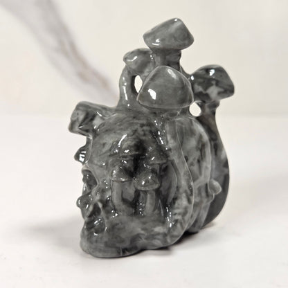 A small glossy gray sculptural figurine with a textured, organic surface, standing on a white surface against a light gray background.