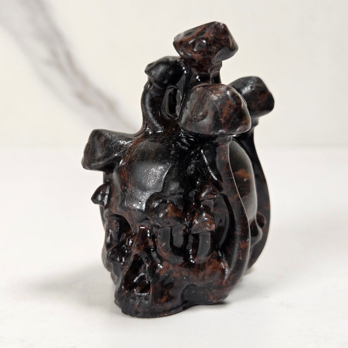 A small dark brown carved figurine depicting a rider on a horse, photographed on a light gray surface with a blurred gray background.