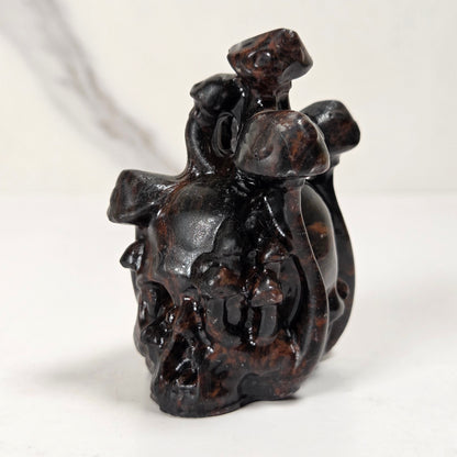 A small dark brown carved figurine depicting a rider on a horse, photographed on a light gray surface with a blurred gray background.