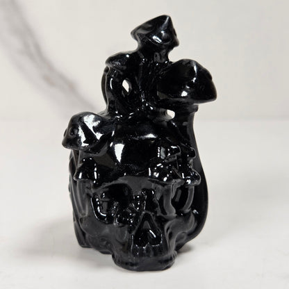 A glossy black skull-shaped decorative object with a small hat on top, photographed against a light neutral background.