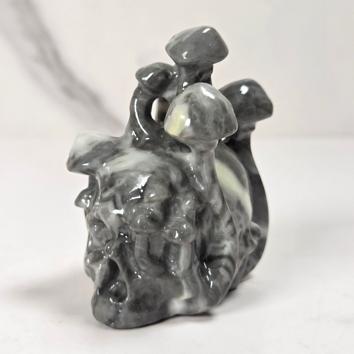 A small carved stone figurine in dark gray and white marbled stone, depicting a stylized face with a mushroom on its head, set against a light gray background.