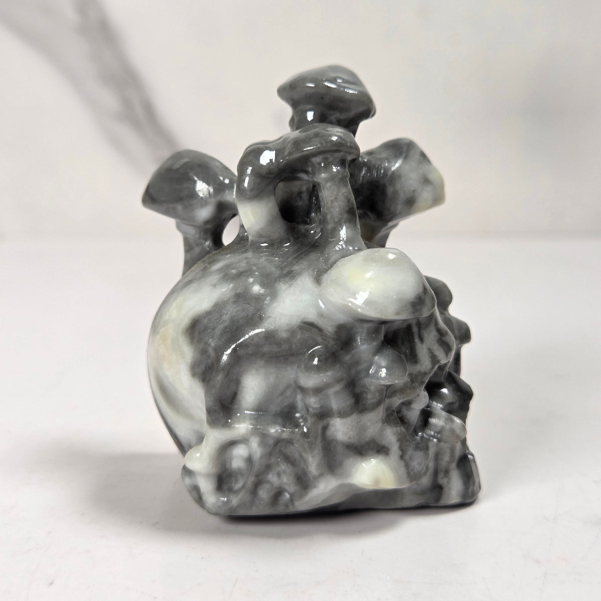 A small carved stone figurine of a mushroom cluster, featuring natural gray, black, and white marbled patterns, set against a light gray background.
