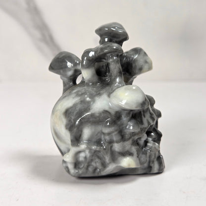 A small carved stone figurine of a mushroom cluster, featuring natural gray, black, and white marbled patterns, set against a light gray background.