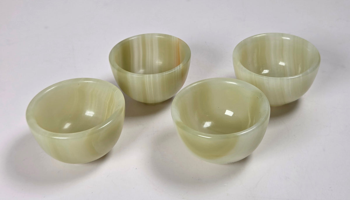 Four small round bowls made of pale green marbled stone, arranged on a plain white surface.