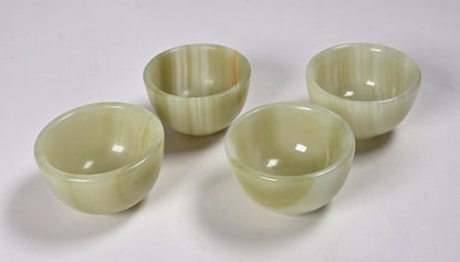 Four small round bowls made of pale green marbled stone, arranged on a plain white surface.