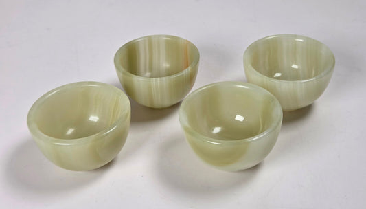 Four small round bowls made of pale green marbled stone, arranged on a plain white surface.