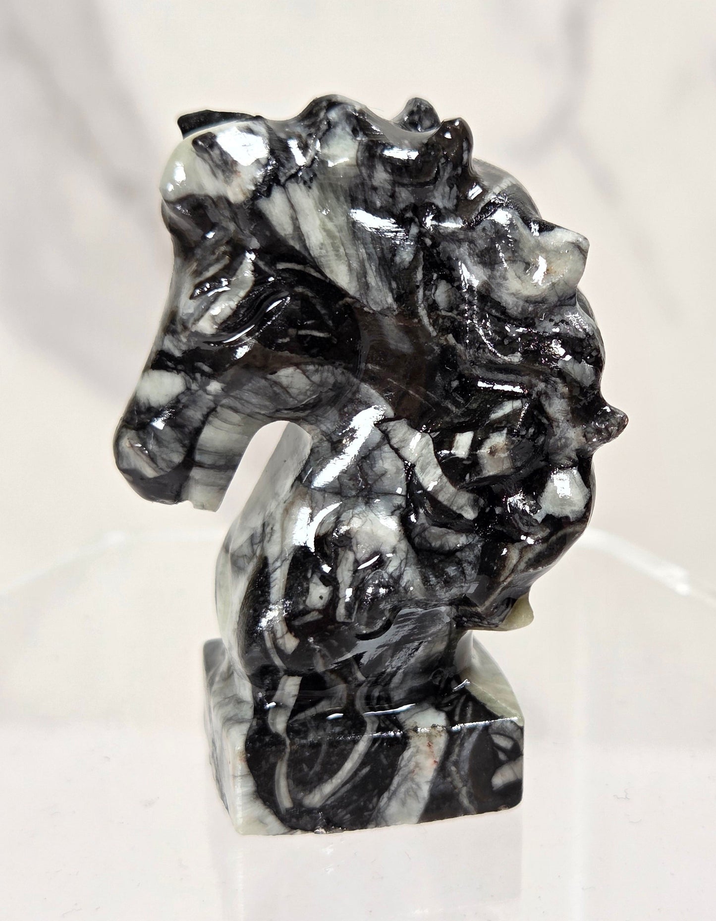 A small carved horse head figurine made of black and white marbled stone, displayed on a clear acrylic stand against a light marble-patterned background.