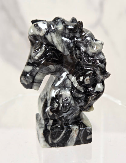 A small carved horse head figurine made of black and white marbled stone, displayed on a clear acrylic stand against a light marble-patterned background.