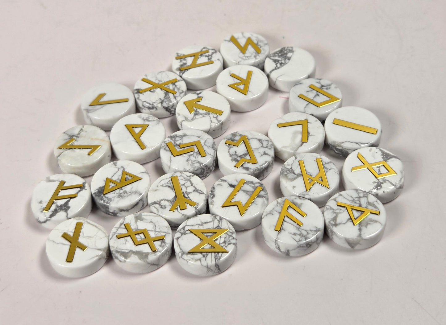 A pile of round white marble-look tokens or pawns with gold runic symbols, arranged on a plain light background.