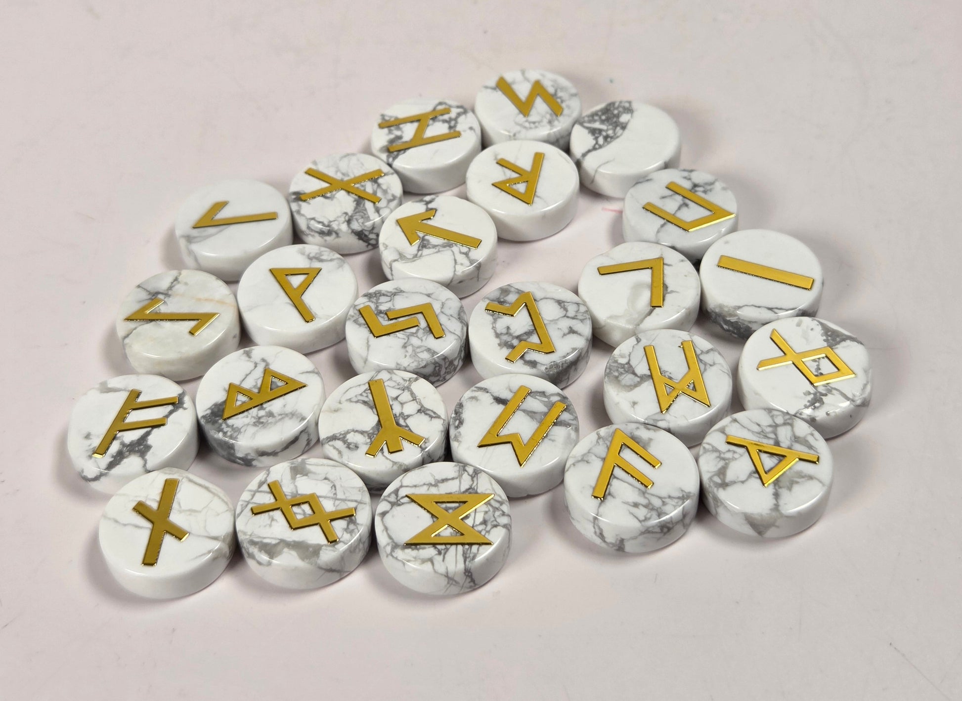 A pile of round white marble-look tokens or pawns with gold runic symbols, arranged on a plain light background.