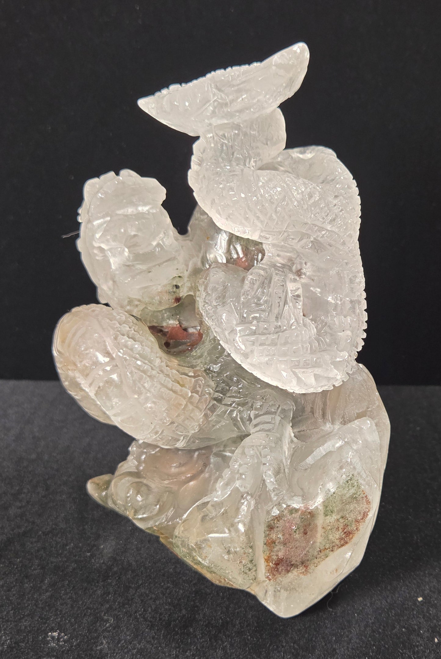 A carved translucent crystal figurine depicting a seated figure with wings, photographed against a dark black background.