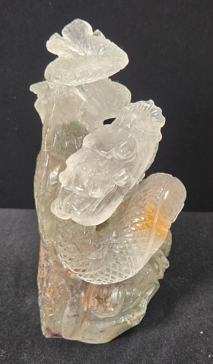 A carved translucent stone sculpture depicting a stylized dragon wrapped around a lotus flower, set against a dark black background.