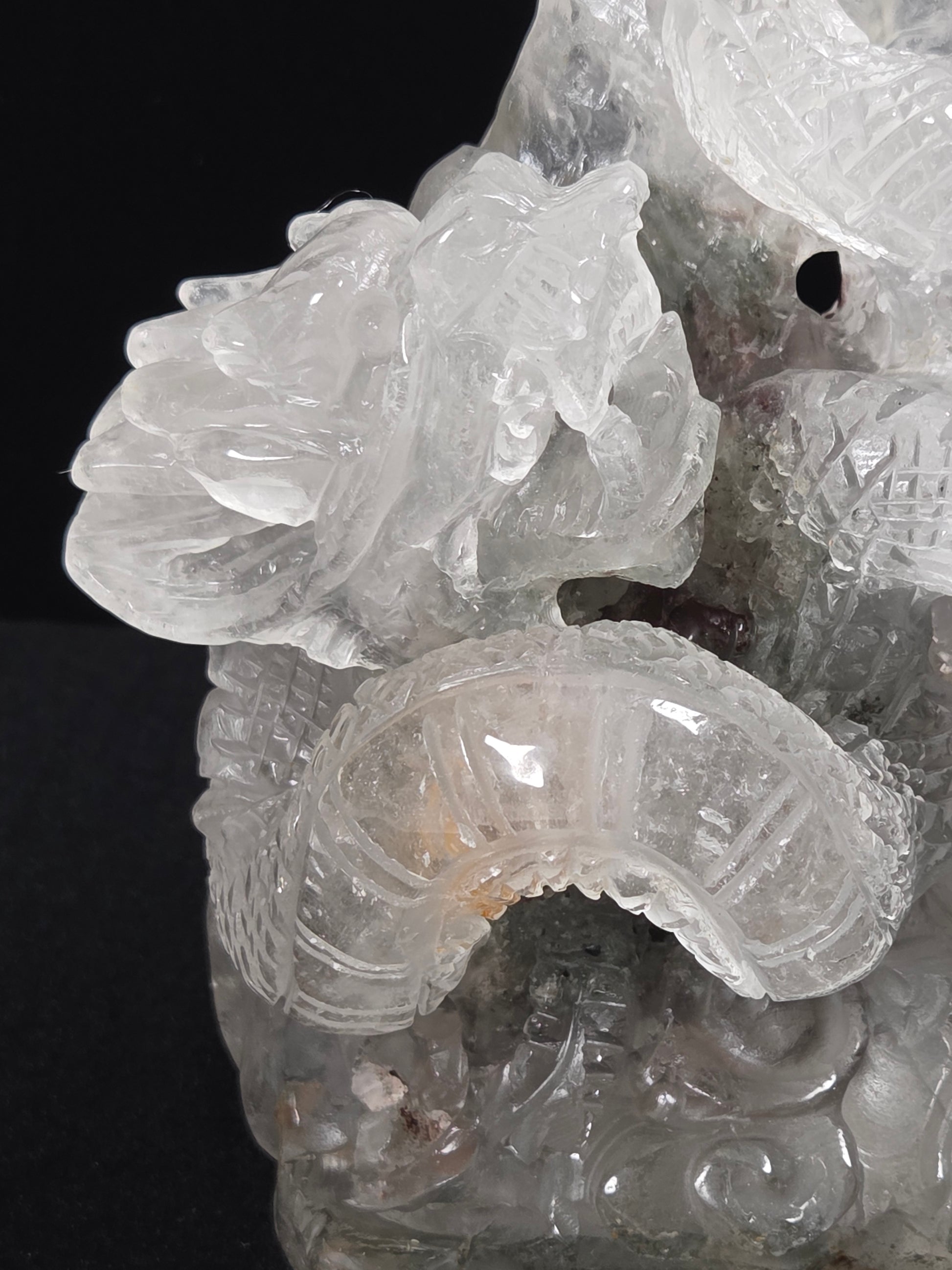 A close-up of a carved translucent stone sculpture, likely quartz, featuring detailed dragon motifs against a solid black background.