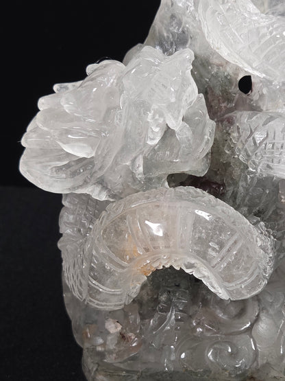 A close-up of a carved translucent stone sculpture, likely quartz, featuring detailed dragon motifs against a solid black background.
