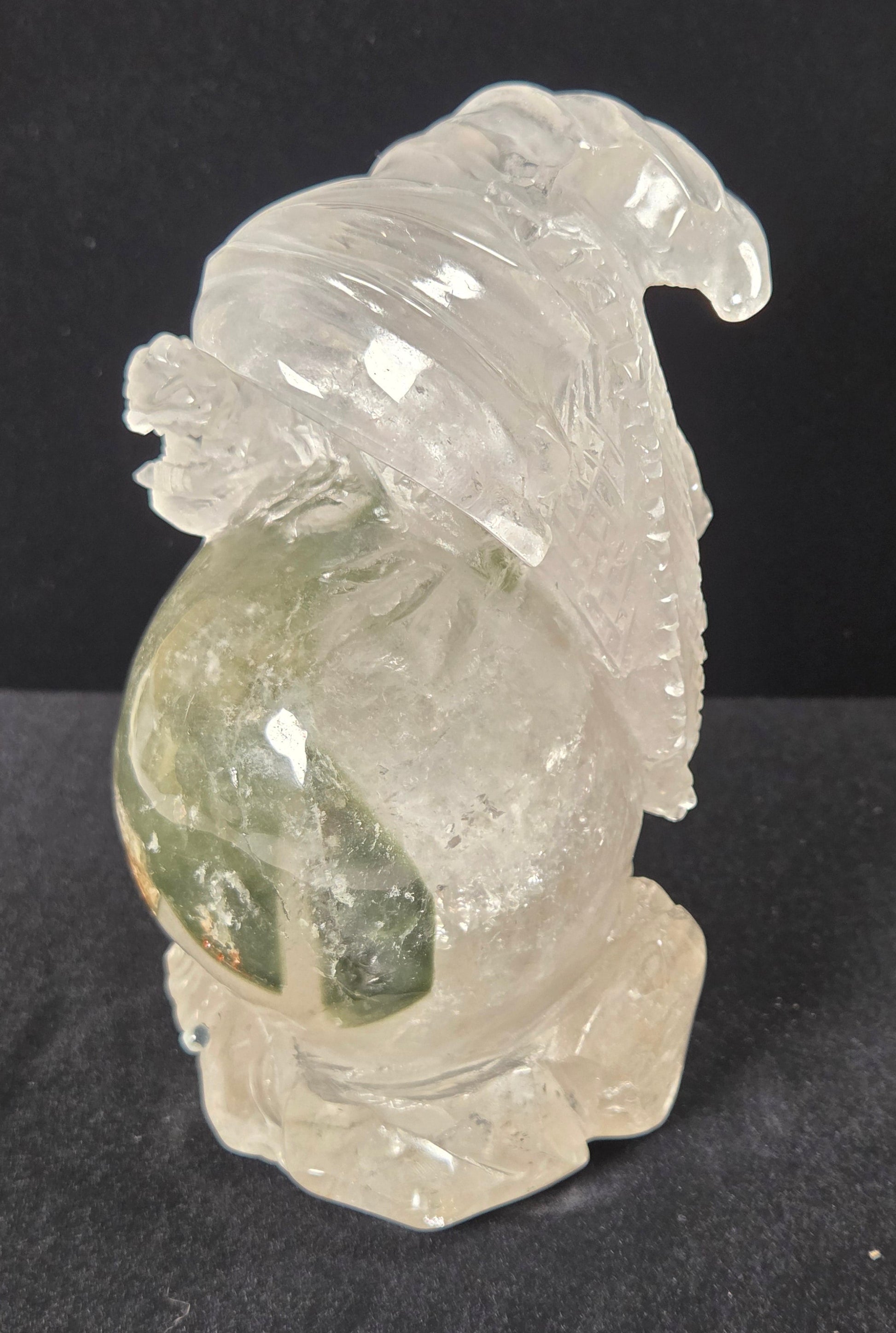 A carved clear crystal figurine depicting a dragon perched on a globe, set against a dark black background.