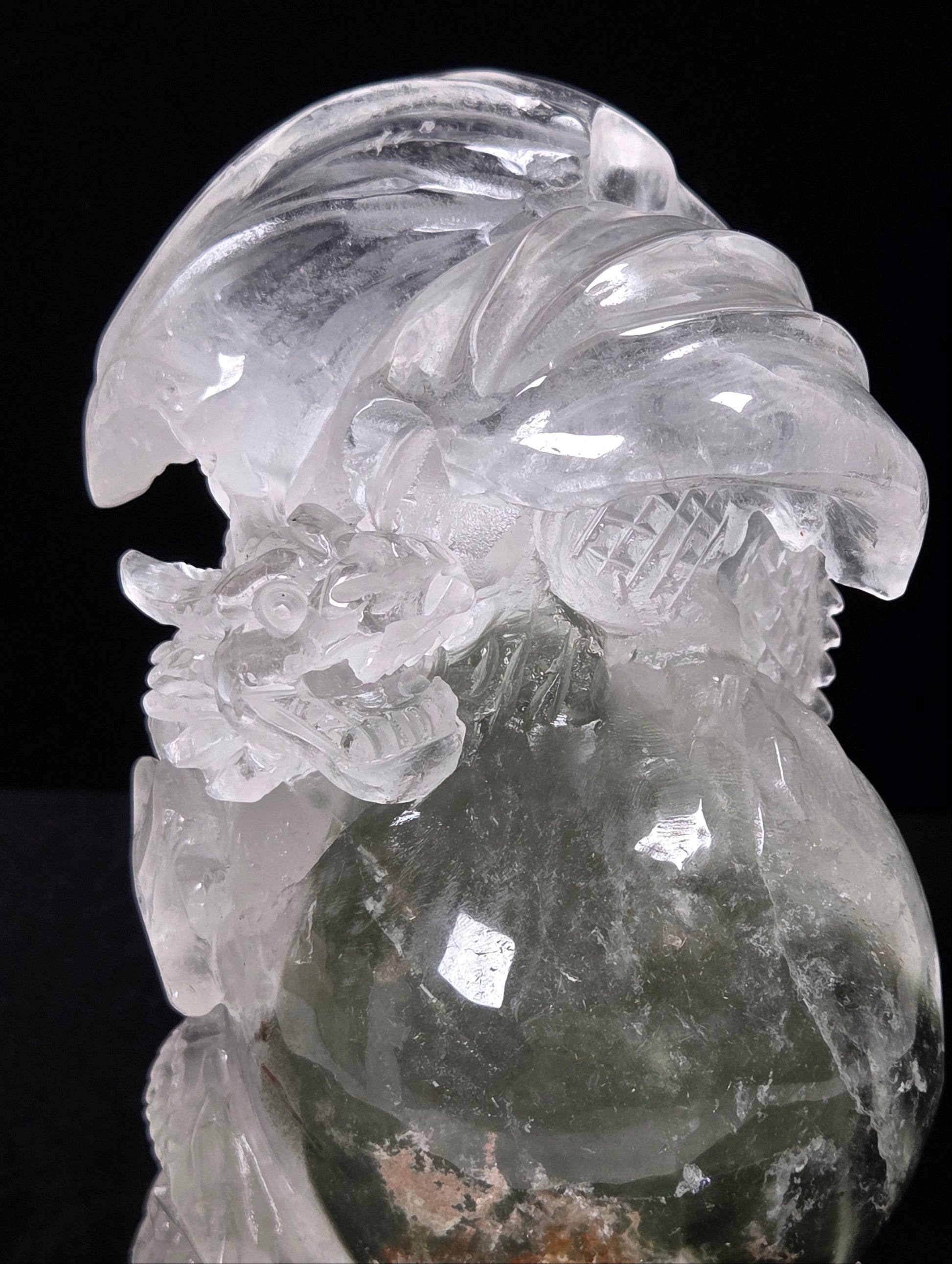 A carved transparent crystal figurine, likely quartz, depicting a stylized bird with a round body and detailed feather and beak features, shown against a solid black background.