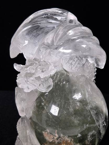 A carved transparent crystal figurine, likely quartz, depicting a stylized bird with a round body and detailed feather and beak features, shown against a solid black background.